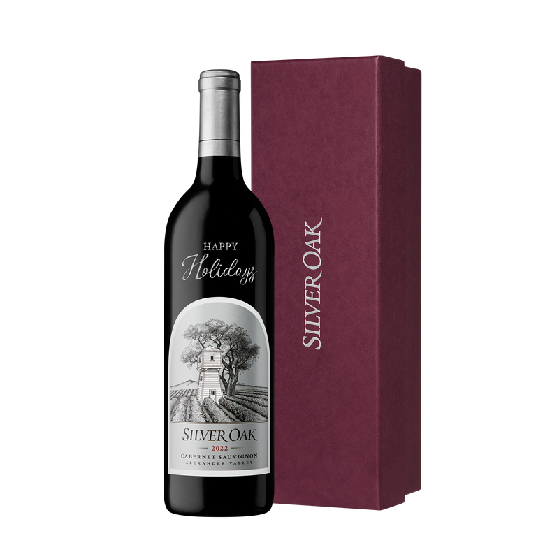 A bottle of Silver Oak Alexander Valley etched and hand painted with the message Happy Holidays, beside a burgundy gift box