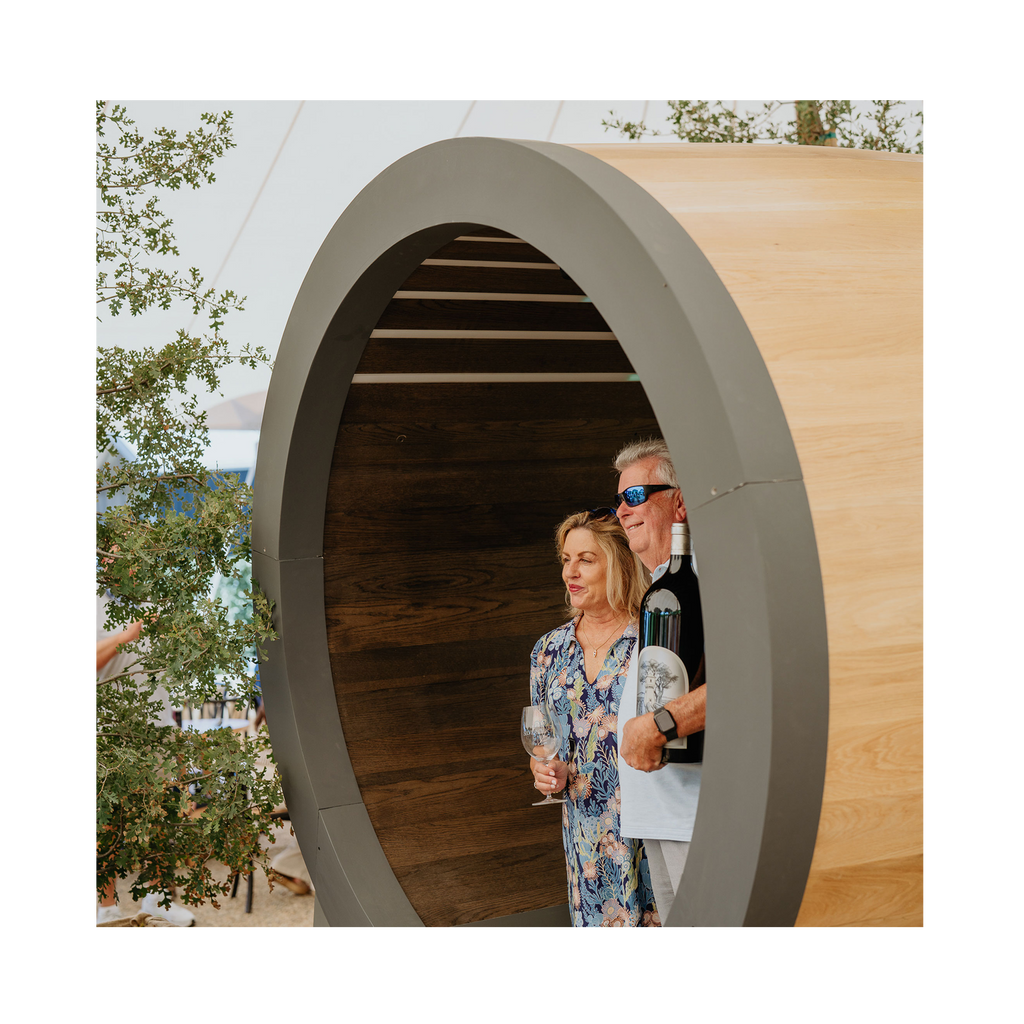 Two people standing inside a wooden barrel with trees in the background