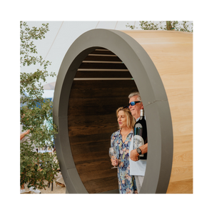 Two people standing inside a wooden barrel with trees in the background