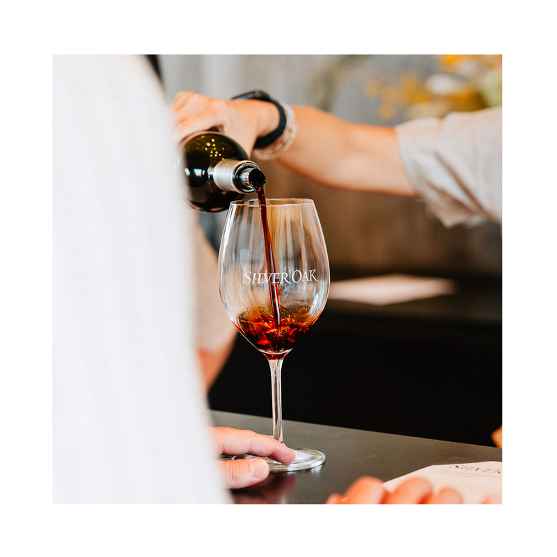 Person pouring red wine into a Silver Oak wine glass.