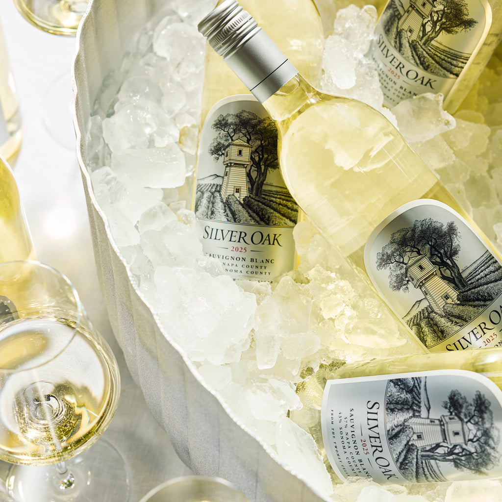 An ice bucked holding a few bottles of Silver Oak Sauvignon Blanc, with wine glasses filled beside